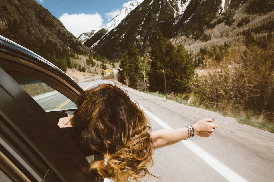 Woman riding on vehicle putting her head and right arm outside the window while travelling the road