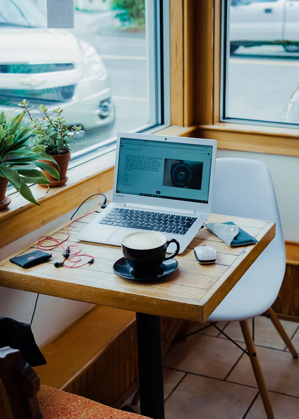 Cup of coffee, laptop computer, and red earphones plugged in laptop on brown wooden table