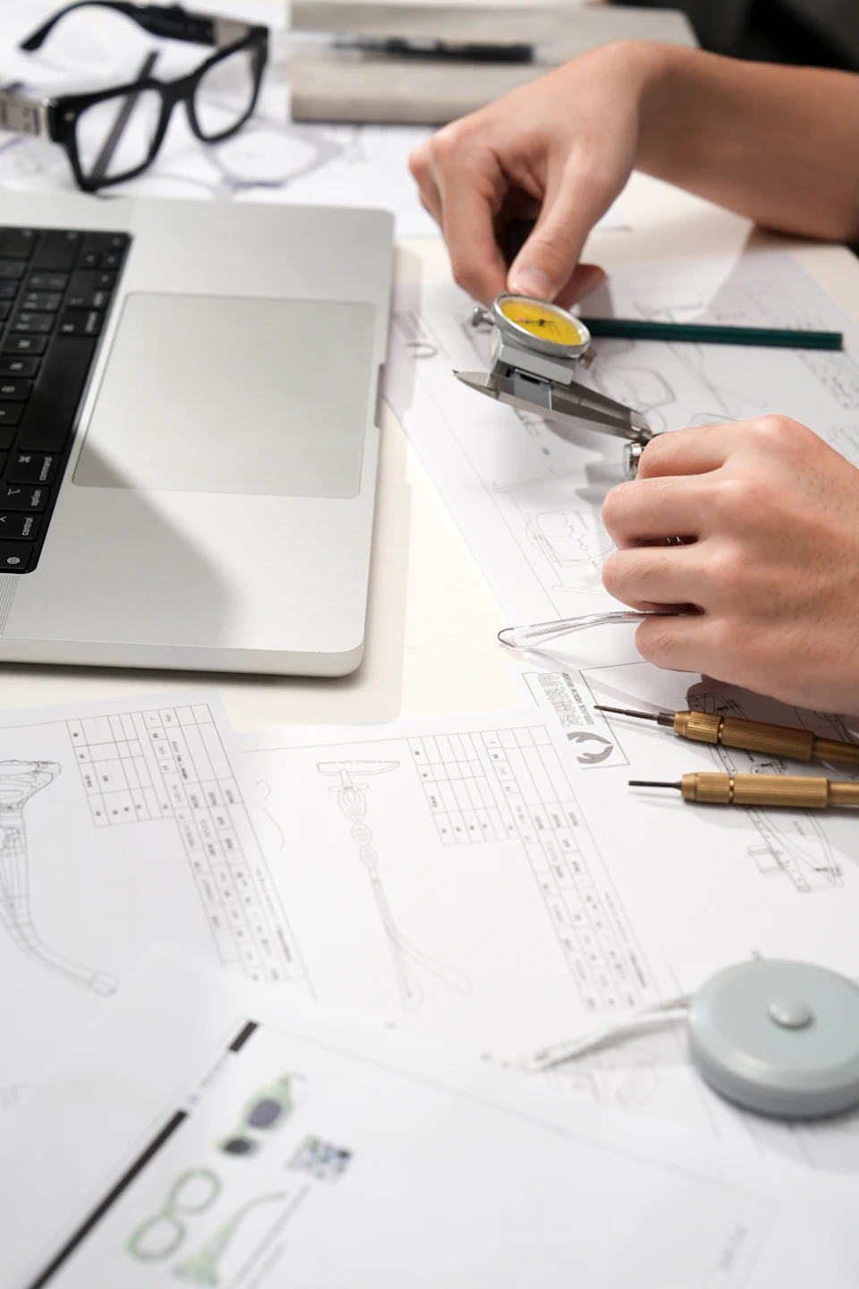 A person using a dial caliper to measure technical drawings on a desk